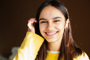 Teenage girl in yellow sweater with braces on top teeth